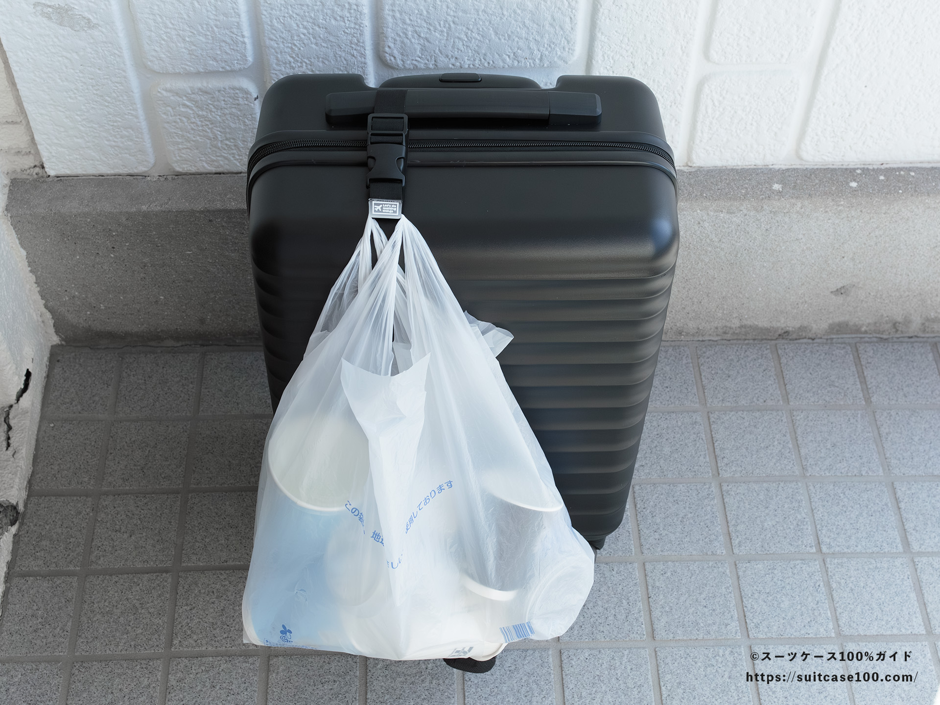 ダイソー スーツケースと手荷物まとめベルト レビュー Sサイズのスーツケースに装着してレジ袋をかけた図 正面 トップハンドルの端に通した状態